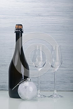 Champagne alcoholic drink, in a black bottle, next to two glass glasses and a Christmas-tree decoration ball, on a light gray