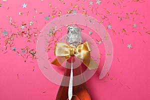 Champagne bottle with bow and glitter on pink background