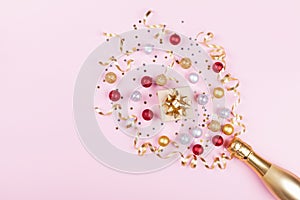 Champagne bottle with confetti stars, gift box and holiday balls on pastel pink background. Christmas pattern. Flat lay style.