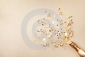 Champagne bottle with confetti stars, glitter and party streamers on golden background. Christmas, birthday or wedding. Flat lay