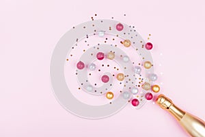 Champagne bottle with confetti stars and holiday balls on pastel pink background. Christmas pattern. Flat lay style