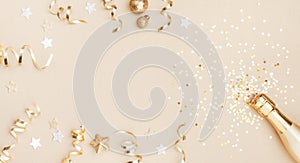 Champagne bottle with confetti stars, holiday decoration and party streamers on gold festive background. Christmas flat lay