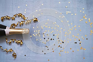 Champagne bottle with confetti stars and party streamers on blue background. Copy space,top view. Flat lay