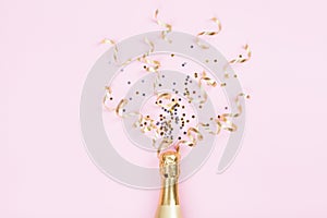 Champagne bottle with confetti stars and party streamers on pink background. Christmas, birthday or wedding concept. Flat lay.