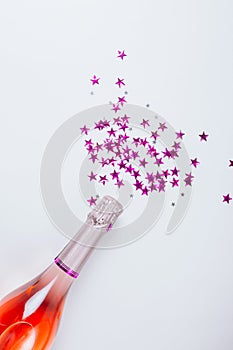 Champagne bottle with confetti stars on white background