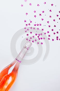 Champagne bottle with confetti stars on white background