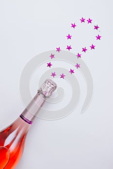 Champagne bottle with confetti stars on white background