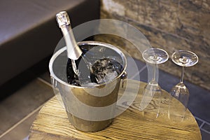 Champagne bottle in cooler, bucket with ice and two champagne glasses on wooden table. romantic dinner and party concept