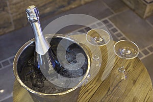 Champagne bottle in cooler, bucket with ice and two champagne glasses on wooden table. romantic dinner and party concept