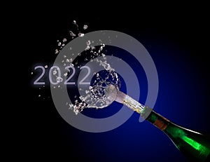 Champagne bottle explosion with cork popping splash and New Year date 2022 against a dark background with blue to black gradient,