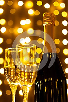 Champagne bottle with glasses of champagne on background with LED lights garland. New year and Christmas. Soft focus.