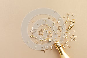 Champagne bottle with gold confetti stars, holiday decoration and party streamers on light festive background. Christmas, birthday