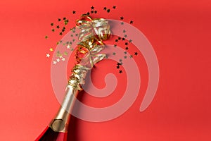 Champagne bottle with golden streamer on red paper background. Valentines day, birthday, wedding celebration concept. Top view.