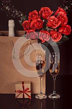 Champagne bottle, red roses in a paper bag and two wine glasses