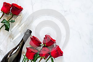 Champagne bottle with two glasses and red roses on marble background