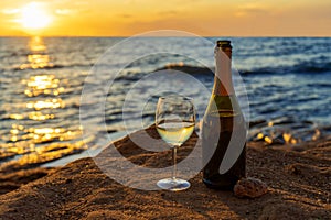 Champagne bottle and wine glass with sparkling wine against amazing sea landscape at sunset. Beautiful still life with alcohol