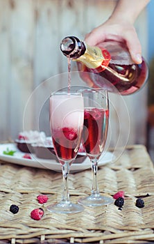 Champagne cocktails with raspberries for a romantic evening on a wooden table. Pink liquid color, glasses with bubbles