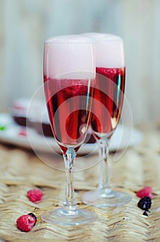 Champagne cocktails with raspberries for a romantic evening on a wooden table. Pink liquid color, glasses with bubbles