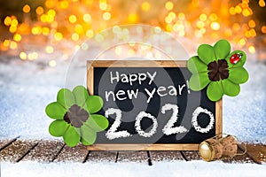 Champagne cork and blackboard with greeting happy new year 2020 wooden planks front of bright golden warm bokeh light background
