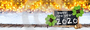 Champagne cork and blackboard with greeting happy new year 2020  wooden planks  front of bright golden warm bokeh light background