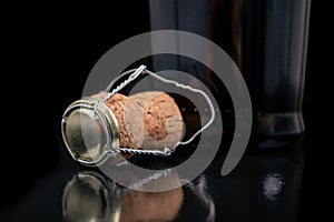 Champagne cork on a dark table. Metal basket and bottle stopper with alcoholic liquor