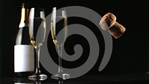 Champagne cork falling in front of two glass flutes and bottle