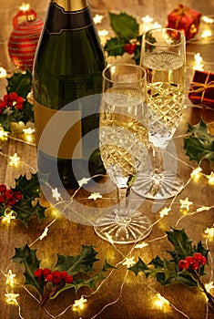 Champagne flutes and bottle with christmas lights, baubles, holly berries and christmas decorations