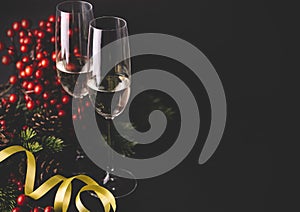 Champagne flutes and christmas decoration with conifer tree, red berries and pinecone on black background. Luxury holiday