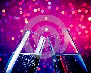 Champagne flutes with gold bubbles on blue tint light bokeh background