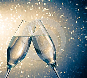 Champagne flutes with golden bubbles on blue light bokeh background