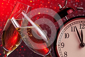 Champagne flutes with golden bubbles on christmas red light bokeh background with vintage alarm clock