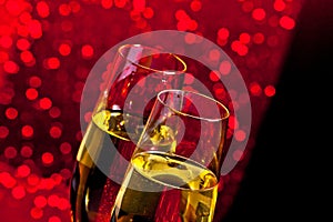 Champagne flutes with golden bubbles on dark red light bokeh background