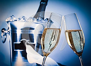 Champagne flutes with golden bubbles in front of champagne bottle in bucket