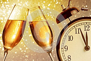 Champagne flutes with golden bubbles on golden light bokeh background with vintage alarm clock