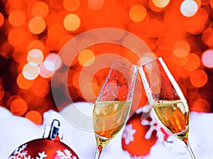 Champagne flutes with golden bubbles on red christmas lights bokeh and balls decoration background