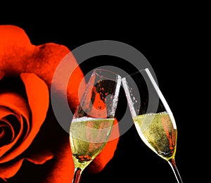 Champagne flutes with golden bubbles on rose flowers and black background