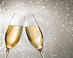 Champagne flutes with golden bubbles on silver light bokeh background