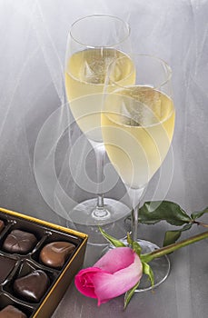 Champagne Flutes, Gourmet Chocolates, and a Pink Rose on Gray Tulle Background