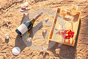 Champagne, fresh strawberry, macaroons, starfishes and seashells on sand beach. Top view