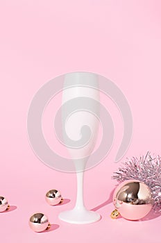 Champagne glass with boubles and shiny decorations. Pink background. New Year eve celebration party concept