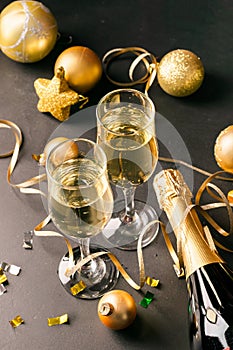 Champagne in glass goblets a bottle of New Year`s toys serpentine stars black background. New year christmas concept.