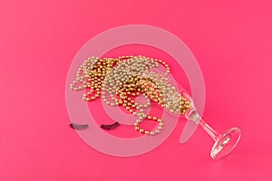 Champagne glass with golden pearls and eyelashes on pink background. Creative minimal New Year paty celebration concept. photo