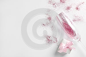 Champagne glass with pink glitter, gift box and space for text on white background. Hilarious celebration