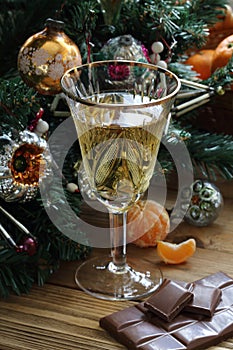 Champagne in a glass, tangerine and chocolate near the New Year`s tree