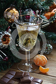 Champagne in a glass, tangerine and chocolate near the New Year`s tree