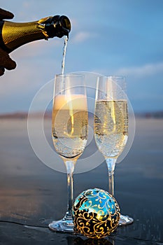 Champagne glasses and a blue Christmas balloon. sparkling wine is poured from a bottle into a glass.