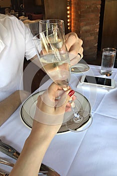 Champagne glasses clink, celebration in a restaurant, man and woman with red manicure holding glasses of champagne making a toast
