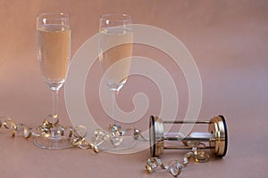 Champagne glasses entwined with ribbon and an hourglass stand on the New Year`s table