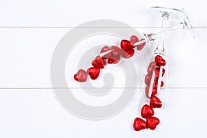 Champagne glasses filled with hearts surrounded by red roses on a white wooden table. Template for Valentine`s Day.