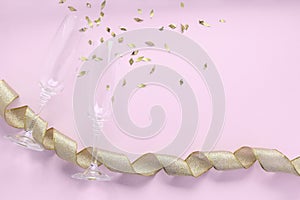 Champagne glasses with golden confetti tinsel and tape on pink background. Celebrate party concept, minimal style. Greeting card